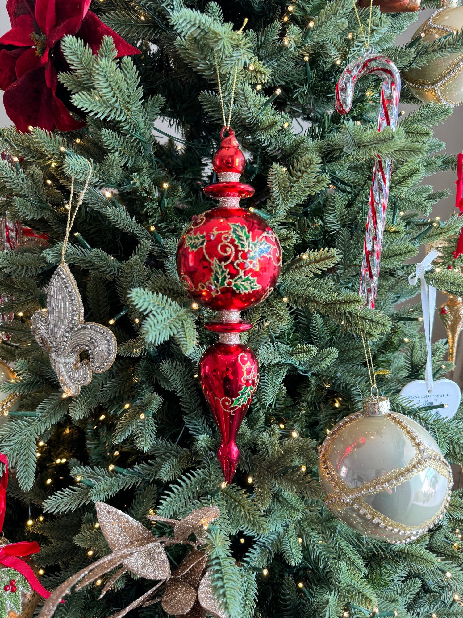 Red finial bauble with holly decoration on a pre lit Christmas tree