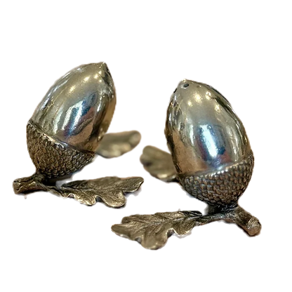 Close-up of polished pewter acorn shakers with textured cups and sculpted oak leaves
