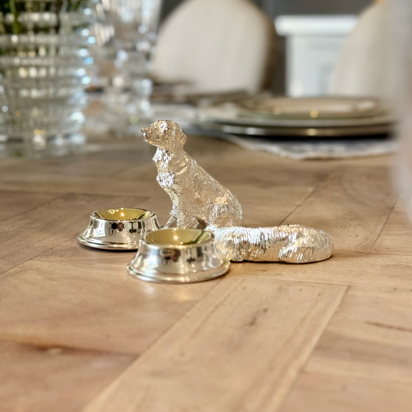 Sitting and lying silver-plated dog salt cruets with small serving bowls on a dining table