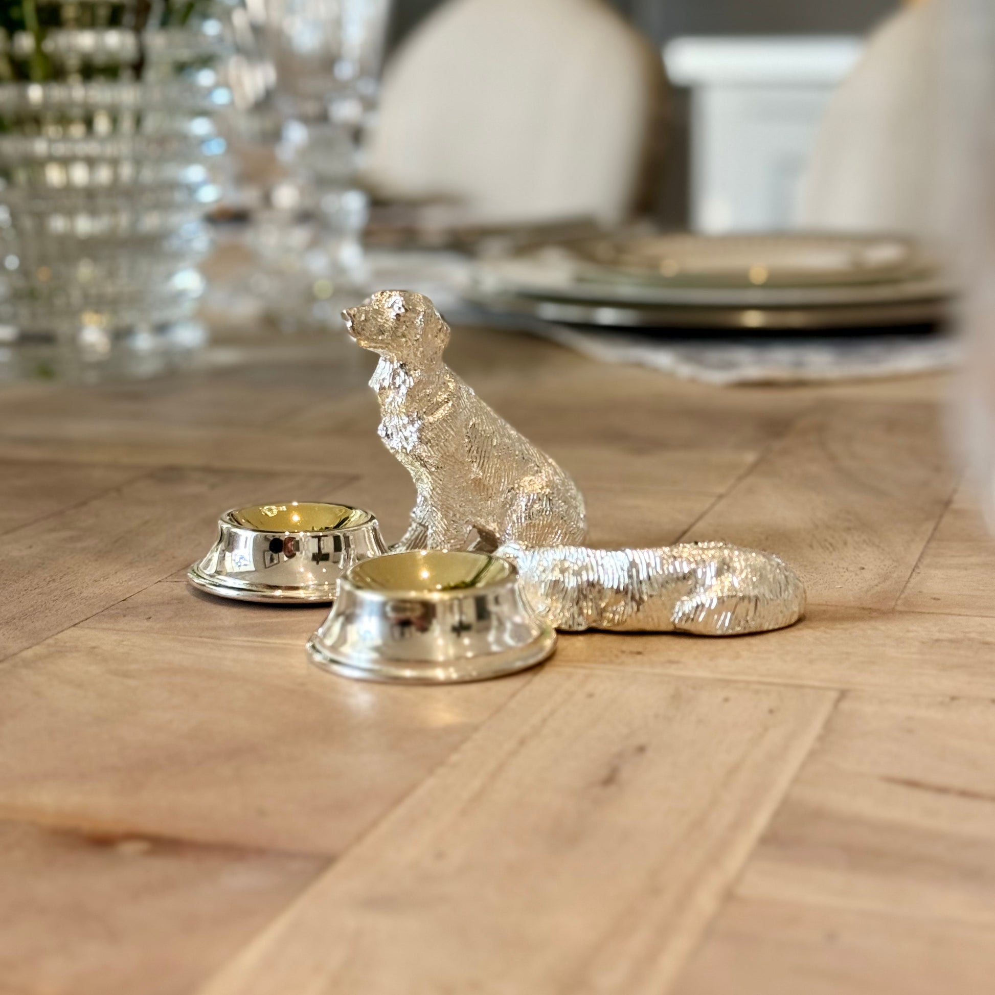 Sitting and lying silver-plated dog salt cruets with small serving bowls on a dining table