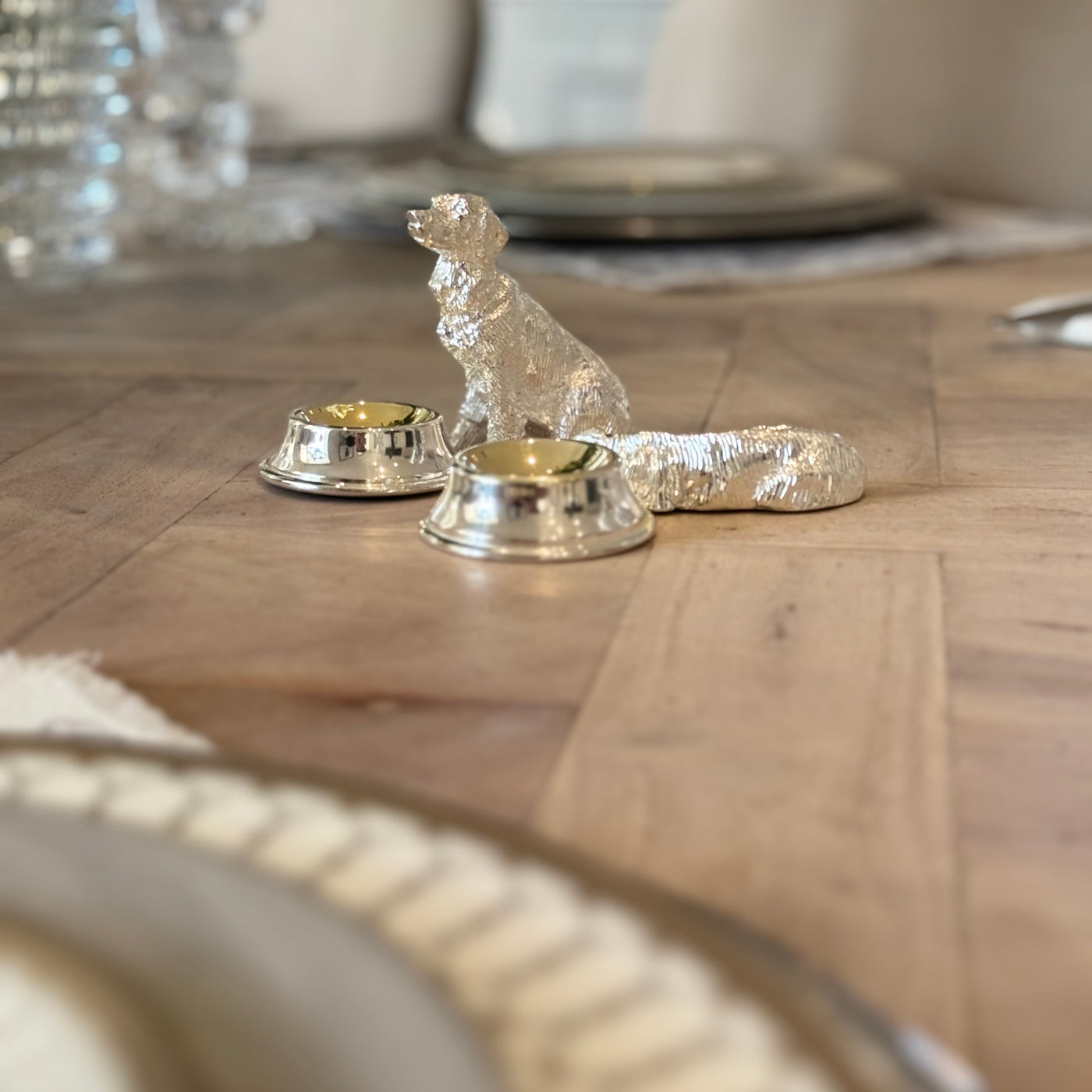 Two silver-plated dog condiment bowls beside a table setting