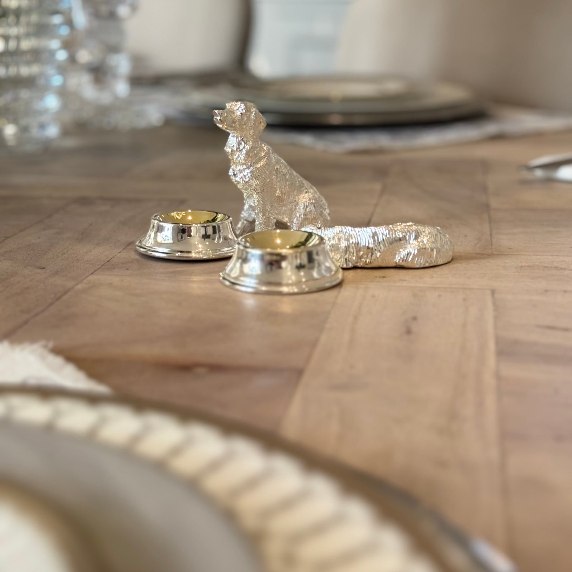 Two silver-plated dog condiment bowls beside a table setting