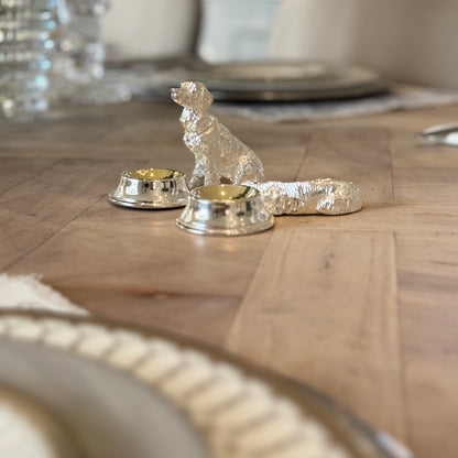 Two silver-plated dog condiment bowls beside a table setting