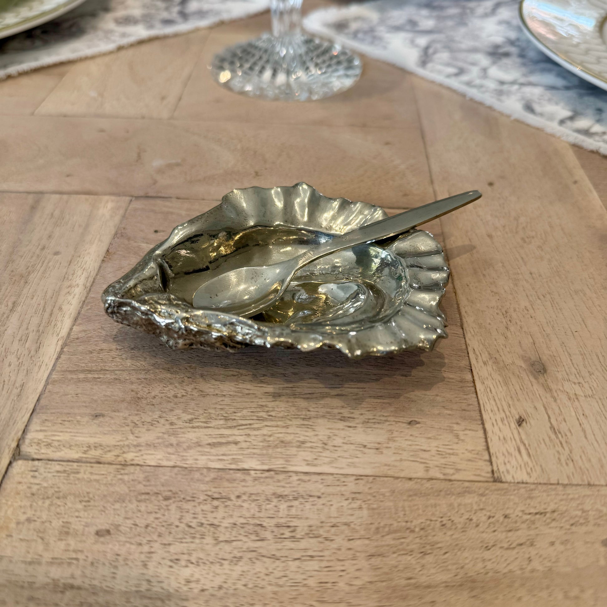 Pewter oyster shell salt cellar and spoon on a wooden dining table