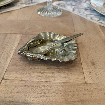Pewter oyster shell salt cellar and spoon on a wooden dining table