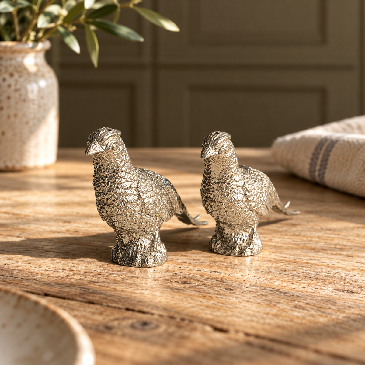 Pair of pewter pheasant salt and pepper shakers on a wooden table in a country kitchen