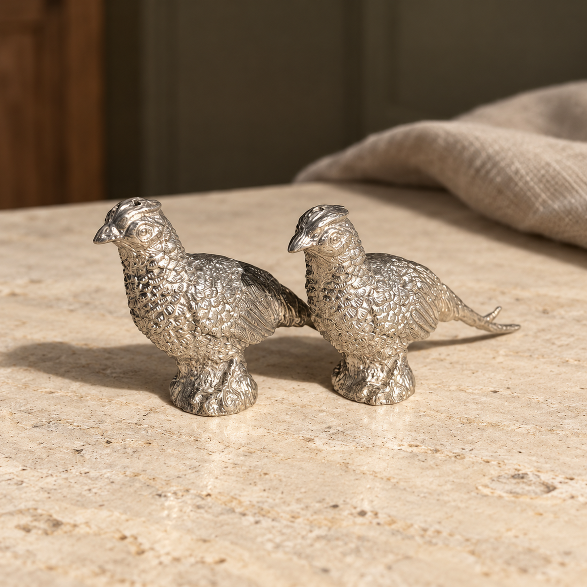 Pewter pheasant shaker pair on pale stone showing detailed feathers and long tails