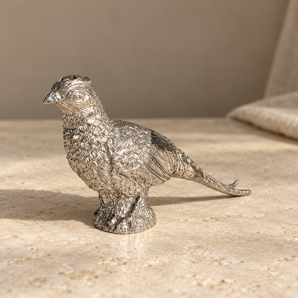 Close-up of a pewter pheasant shaker on pale limestone showing feather and tail detail