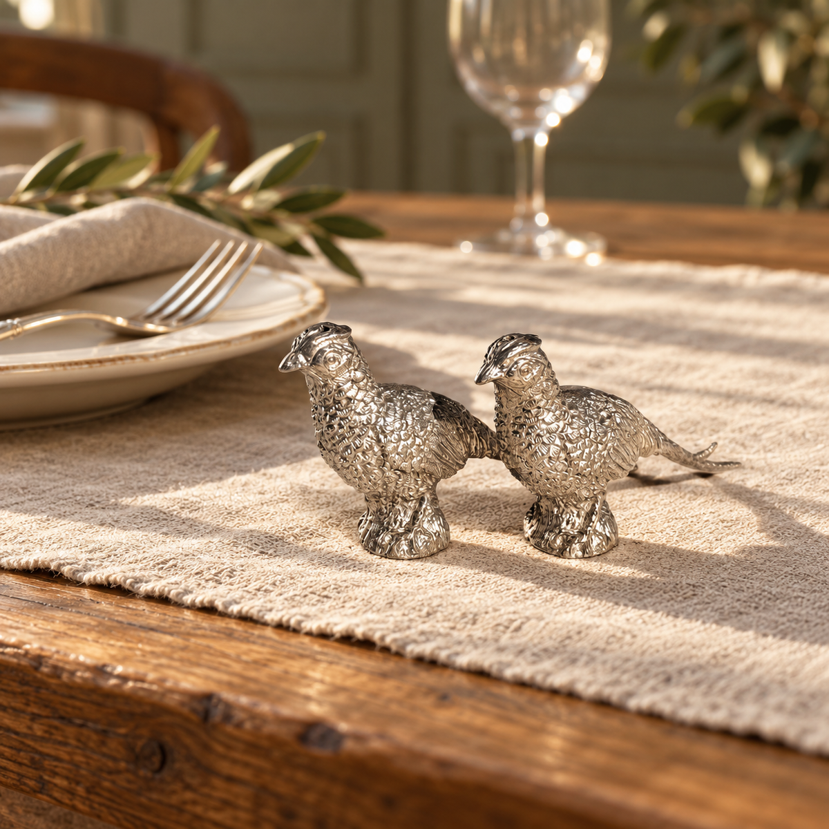 Pewter pheasant salt and pepper shakers on a linen runner beside a place setting