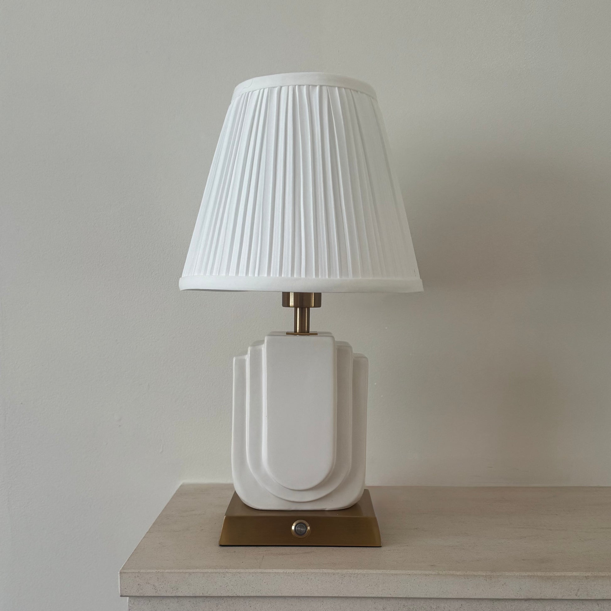 Belgravia rechargeable table lamp lit with warm glow, handmade white ceramic base and pleated shade