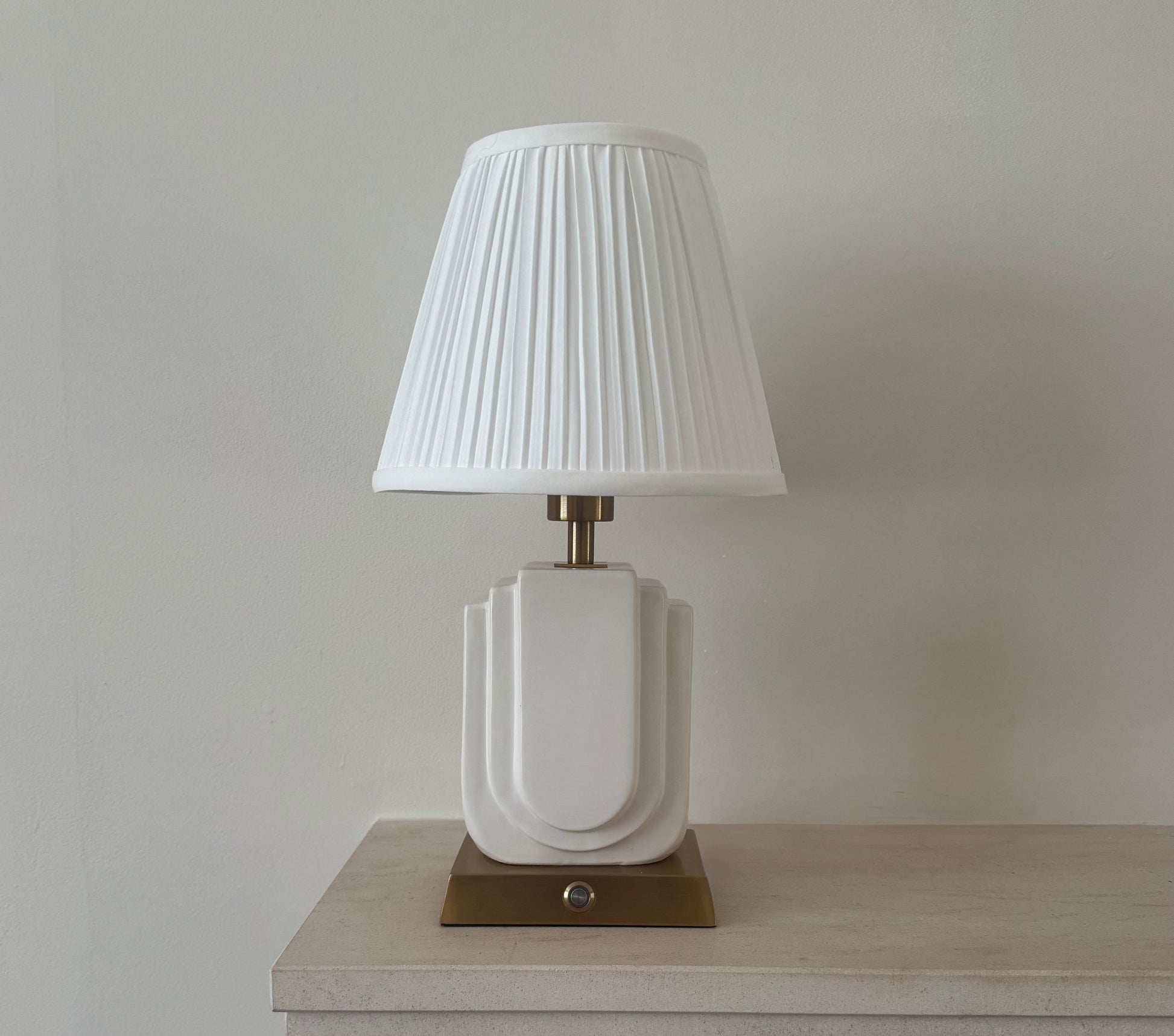 Belgravia rechargeable table lamp lit with warm glow, handmade white ceramic base and pleated shade